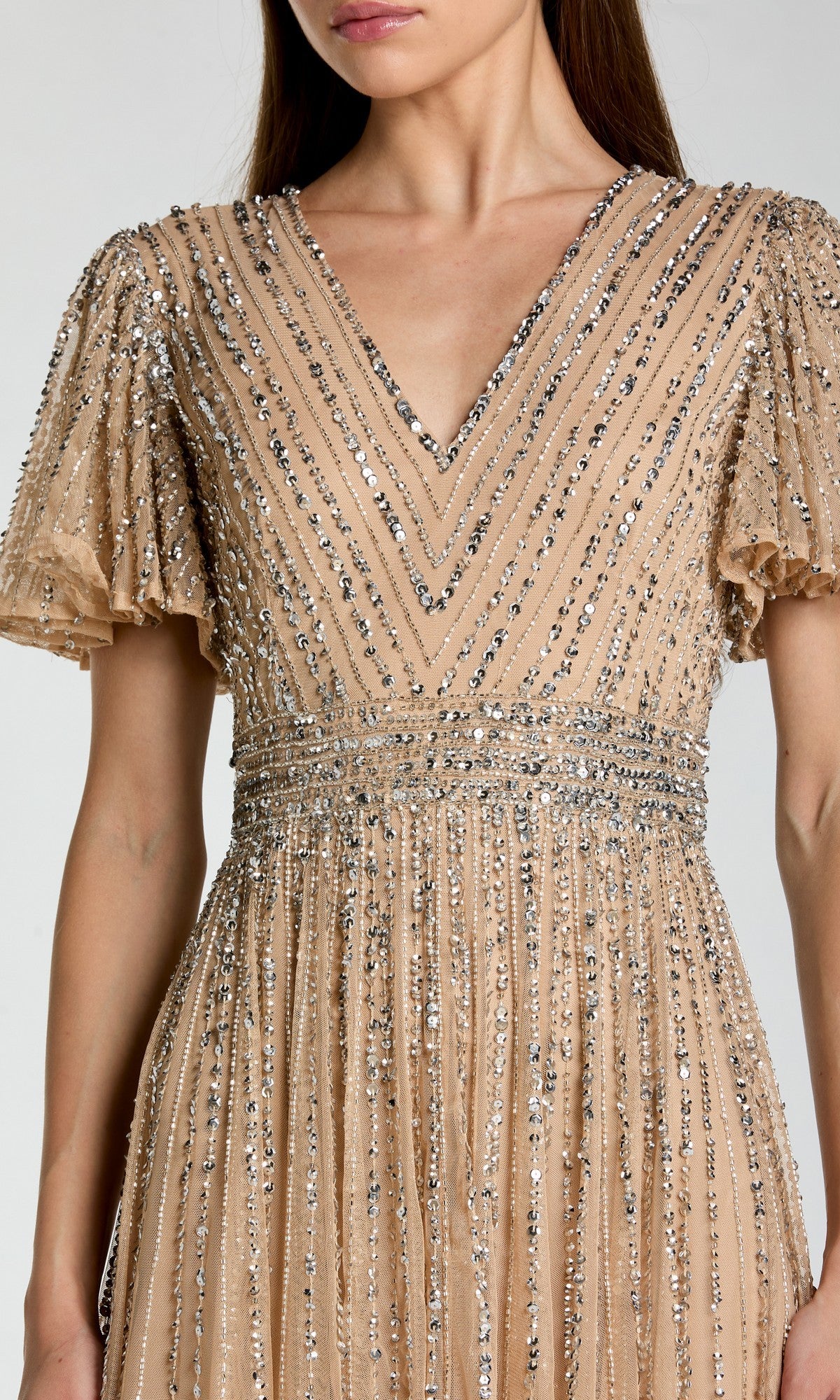 A woman wearing the Long Formal Dress: Mac Duggal 5713, a beige evening gown featuring short flutter sleeves and silver sequin embellishments arranged in vertical and chevron patterns.